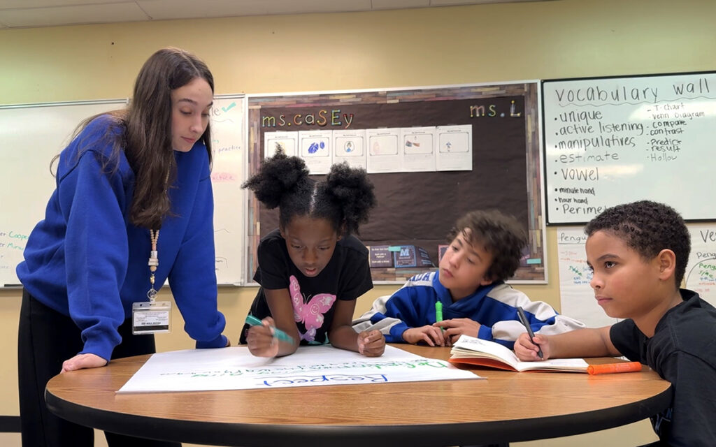 A University of South Florida education student works with three Pepin Academies students during a small-group classroom activity, providing individualized instruction and collaborative learning support.
