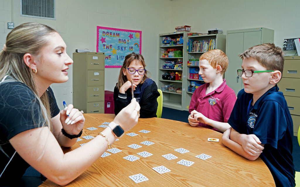 A Pepin Academies staff member leads a small group of elementary students with learning disabilities in an interactive card game, supporting communication, critical thinking, and social skills in a classroom setting.