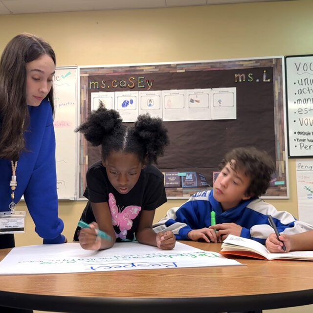 A University of South Florida education student works with three Pepin Academies students during a small-group classroom activity, providing individualized instruction and collaborative learning support.