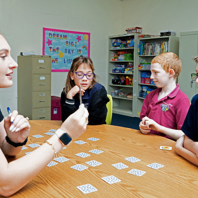 A Pepin Academies staff member leads a small group of elementary students with learning disabilities in an interactive card game, supporting communication, critical thinking, and social skills in a classroom setting.