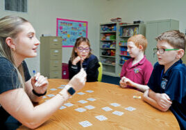 A Pepin Academies staff member leads a small group of elementary students with learning disabilities in an interactive card game, supporting communication, critical thinking, and social skills in a classroom setting.